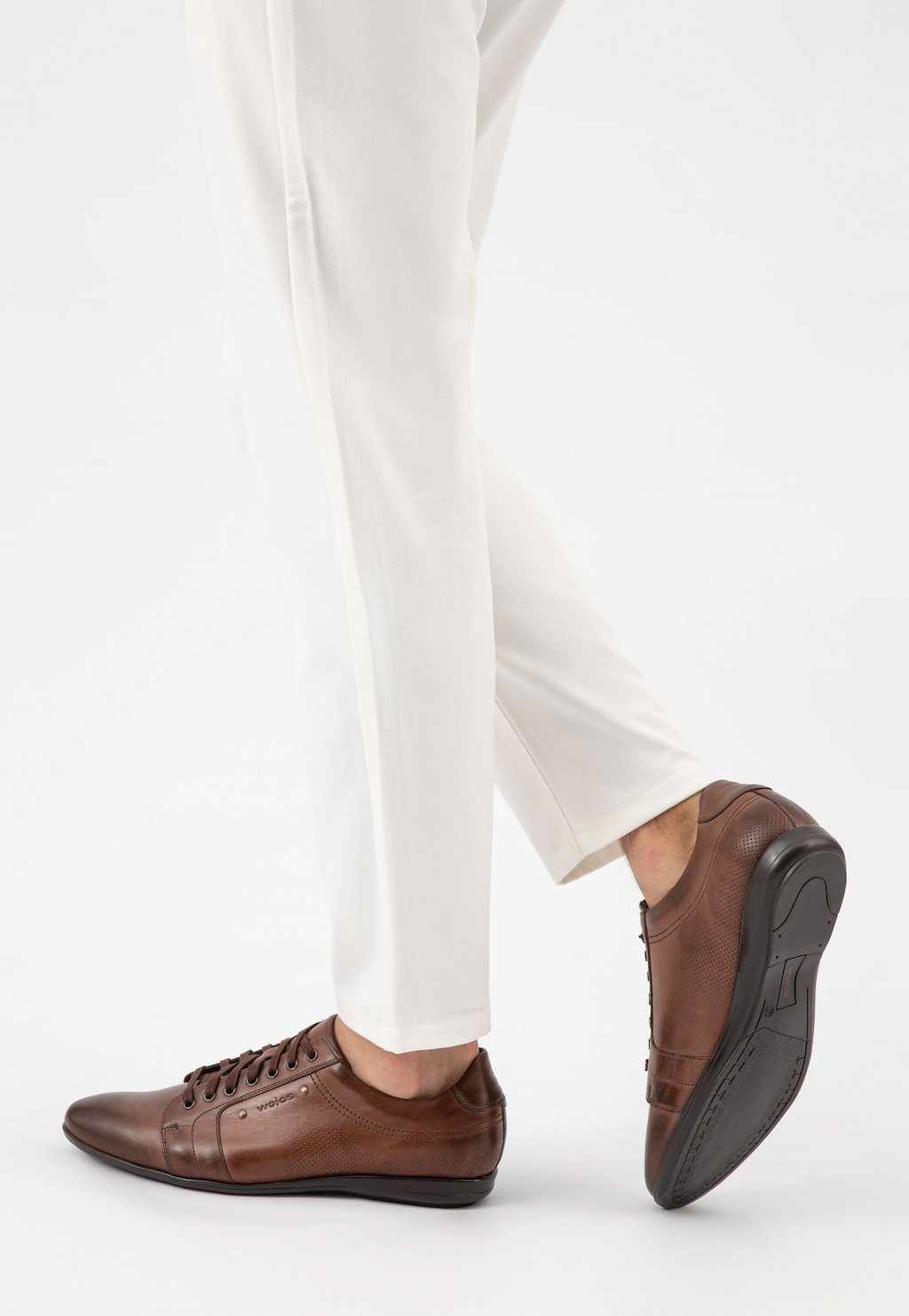 Brązowe półbuty męskie Wojas model 7004-52 prezentowane na nogach osoby w białych spodniach, widok z boku ukazujący klasyczny design i perforowaną skórzaną cholewkę.