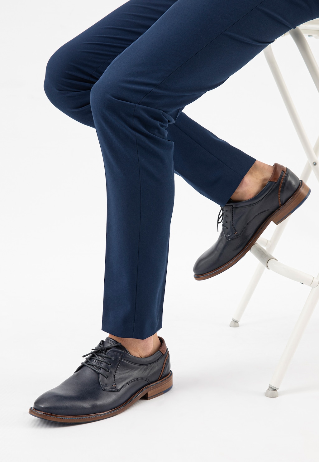 Eleganckie granatowe półbuty męskie Wojas model 9071-56 ze skóry, widoczne na nogach mężczyzny w granatowych spodniach, siedzącego na białym krześle.