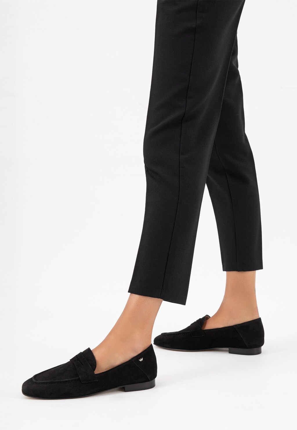 Czarne zamszowe mokasyny damskie Wojas model 46227-61 na płaskiej podeszwie zestawione z eleganckimi czarnymi spodniami, widok z boku pokazujący stylowy profil butów.
