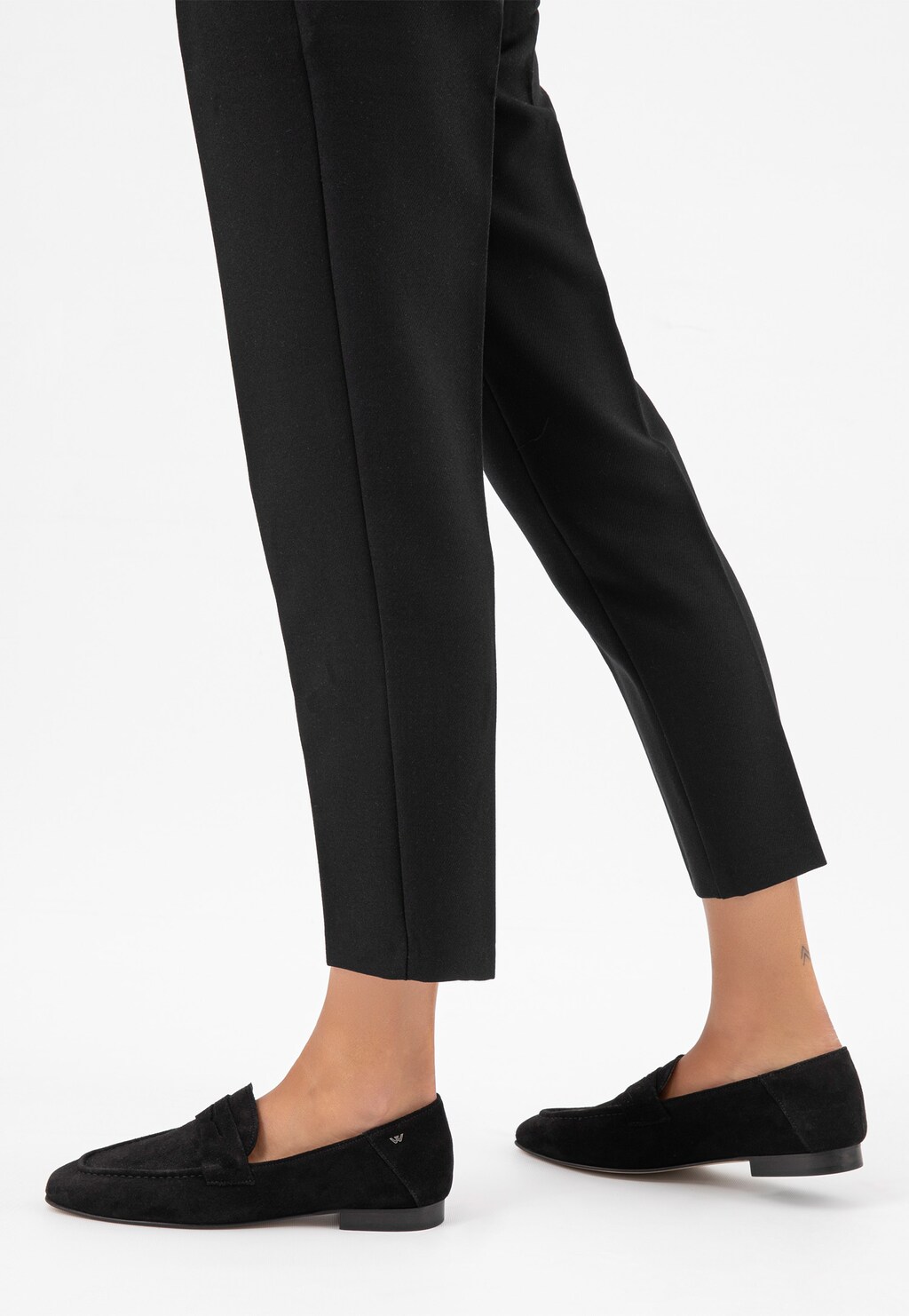 Czarne mokasyny damskie Wojas 46227-61 na płaskiej podeszwie, prezentowane na stopach modelki ubranej w eleganckie czarne spodnie.