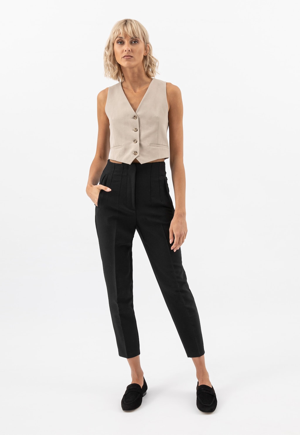 Model w eleganckim stroju z jasną kamizelką i czarnymi spodniami, prezentująca czarne mokasyny damskie Wojas model 46227-61 na płaskiej podeszwie w stylizacji biurowej.