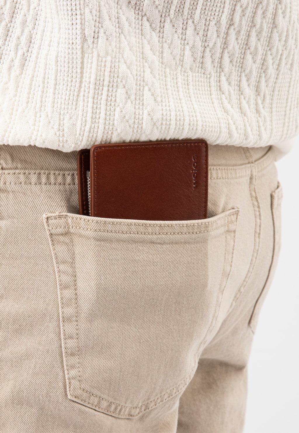 Jasnobrązowy skórzany portfel męski Wojas model 91072-53 wystający z tylnej kieszeni beżowych spodni, osoba ma na sobie biały sweter z dzianiny.