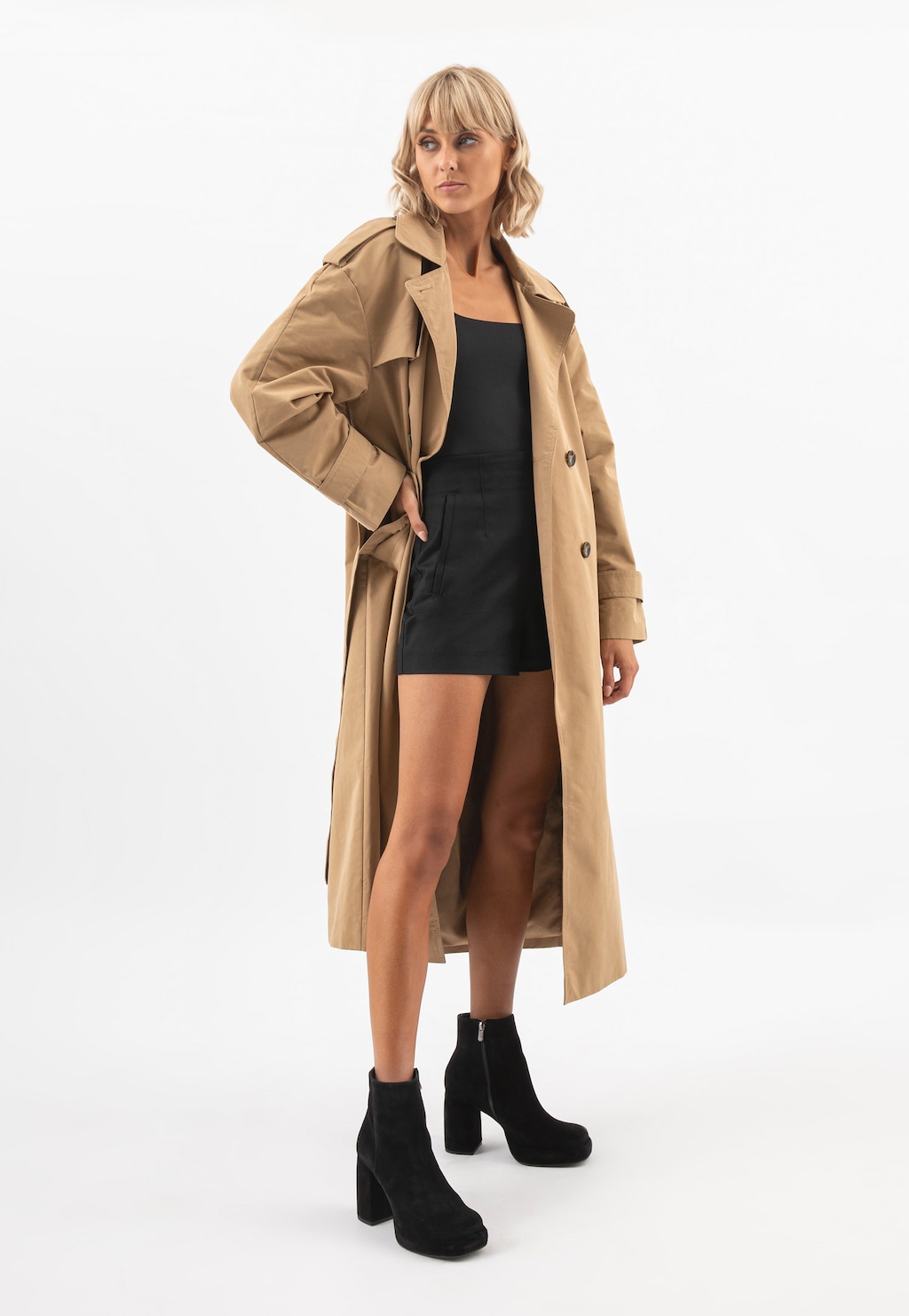 Modelka w beżowym płaszczu i czarnej sukience prezentująca czarne botki damskie Wojas model 55202-61 na słupku z dwoiny welurowej, widoczne z przodu.