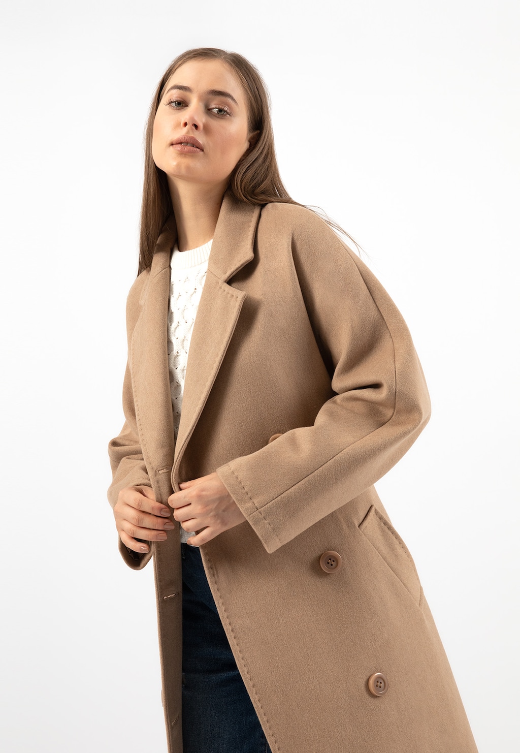 Elegancki długi płaszcz damski RELAKS R99015-44 w kolorze beżowym z szerokimi klapami, zapinany na guziki, prezentowany na modelce w białym swetrze.