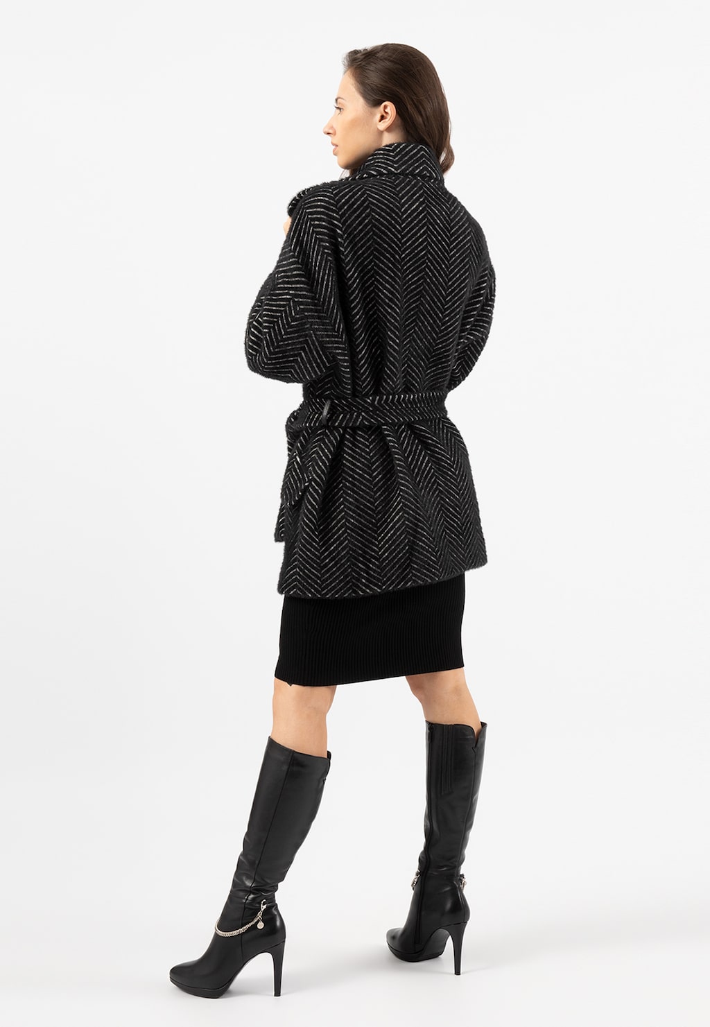 Czarny puchaty płaszcz RELAKS model R9902341 z jodełkowym wzorem, widok z tyłu. Stylizacja z czarną spódnicą i wysokimi kozakami na obcasie.