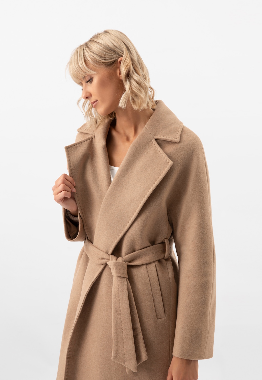 Długi brązowy płaszcz RELAKS model R99017-44 z szerokim kołnierzem i paskiem w talii, prezentowany z profilu na modelce z blond włosami.