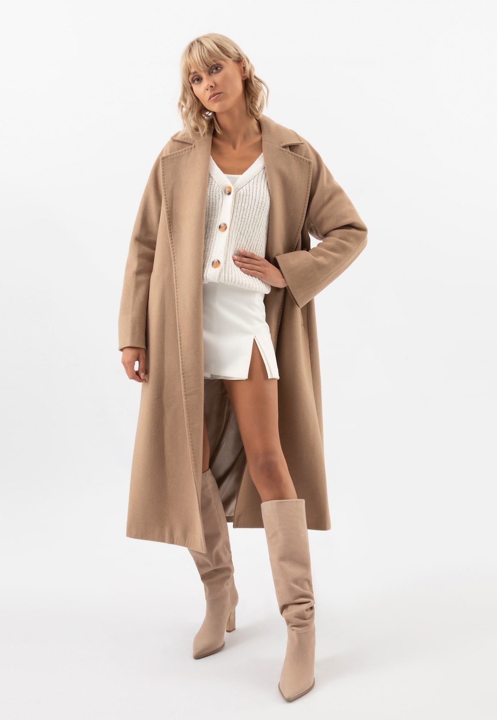 Elegancki długi brązowy płaszcz RELAKS R99017-44 prezentowany na modelce, noszony z białym swetrem, mini spódniczką i dopasowanymi beżowymi kozakami marki Relaks.