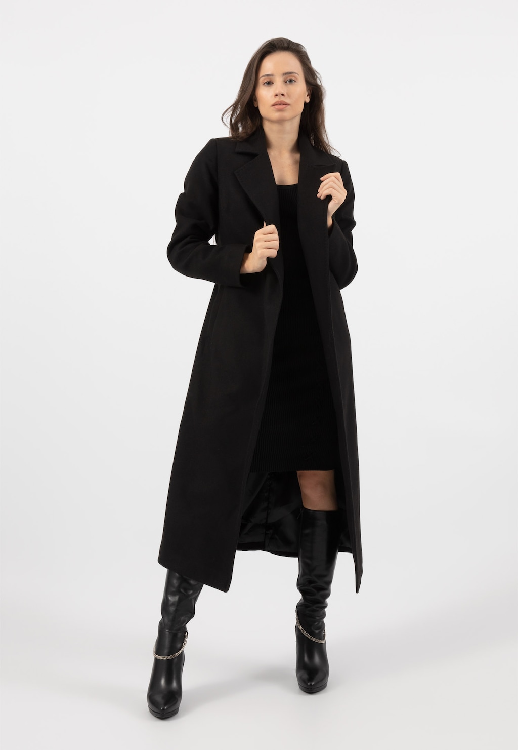 Elegancki czarny płaszcz damski Relaks R99018-41 prezentowany na modelce w stylizacji z czarną sukienką i wysokimi kozakami. Klasyczny, długi fason z wyraźnym kołnierzem.