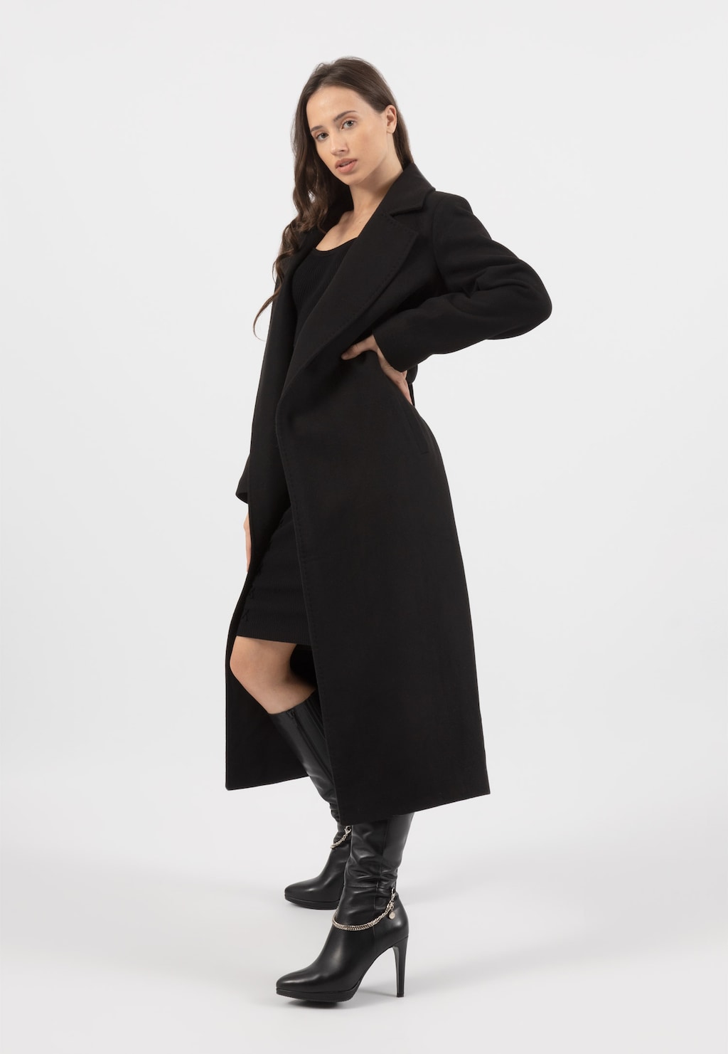 Elegancki czarny płaszcz damski RELAKS model R99018-41 prezentowany na modelce. Długi, gładki fason z wyraźnym kołnierzem, w zestawie z czarną sukienką i wysokimi butami.