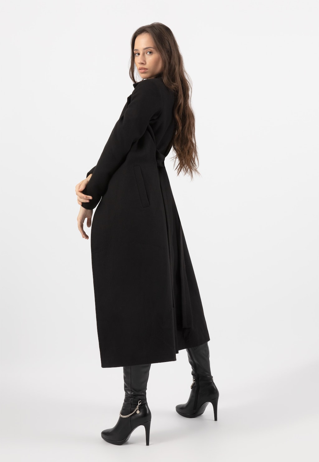 Elegancki czarny płaszcz damski RELAKS model R99018-41 prezentowany z tyłu, długi krój, widoczne kieszenie, w stylizacji z czarnymi skórzanymi butami na obcasie.