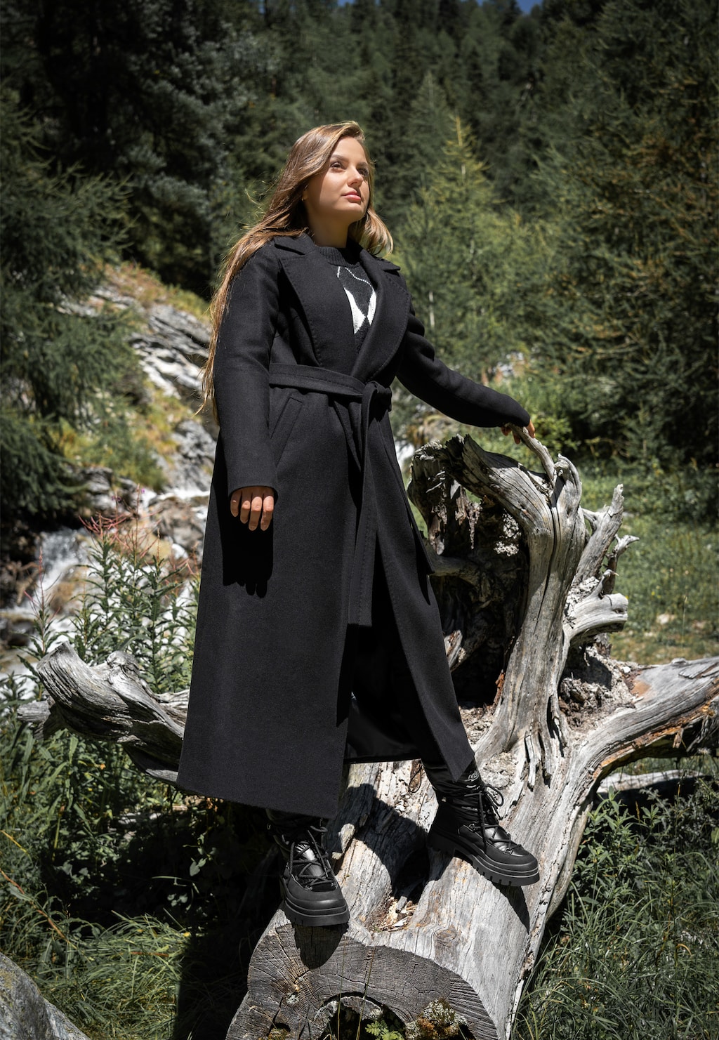 Elegancki czarny płaszcz damski Relaks R99018-41 z paskiem, prezentowany w górskim otoczeniu. Model noszony z czarnymi butami marki Relaks na tle zielonych drzew.