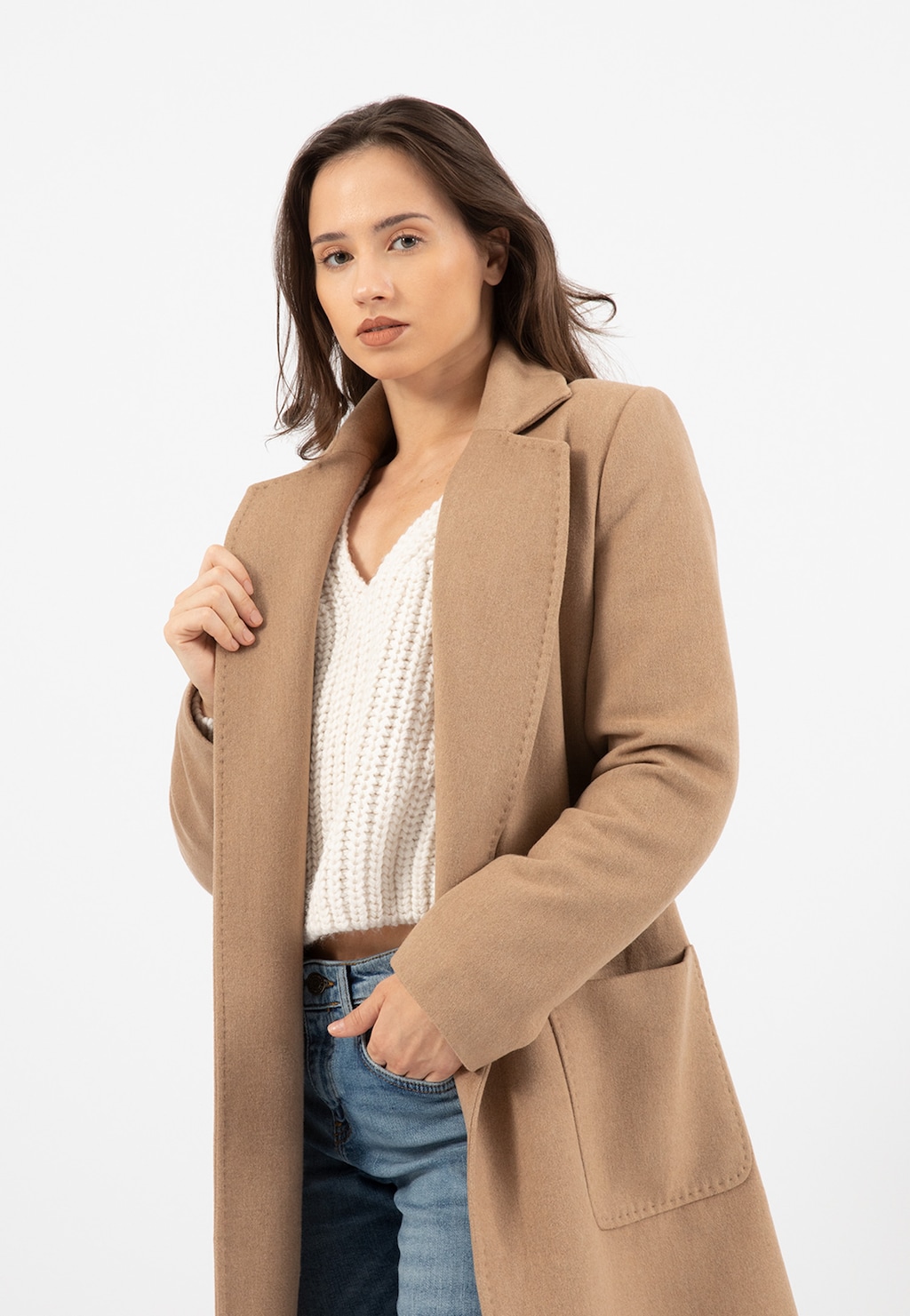 Elegancki beżowy płaszcz RELAKS model R99020-44 prezentowany na modelce, zestawiony z białym swetrem i jeansami. Stylowa propozycja na sezon jesienno-zimowy.