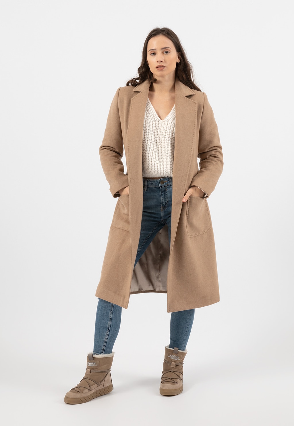 Elegancki beżowy płaszcz damski RELAKS model R99020-44 prezentowany na modelce w stylizacji z białym swetrem, jeansami i beżowymi butami śniegowcami marki Relaks.