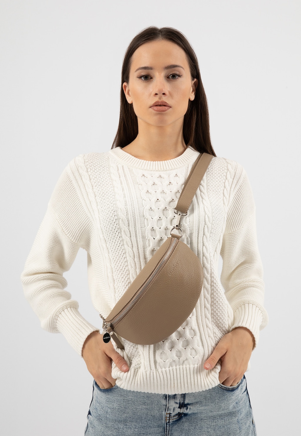 Beżowa nerka Wojas 80099-54 z naturalnej skóry licowej prezentowana na modelce w białym swetrze. Torebka na pasku z dekoracyjnym suwakiem, idealna do casualowych stylizacji.