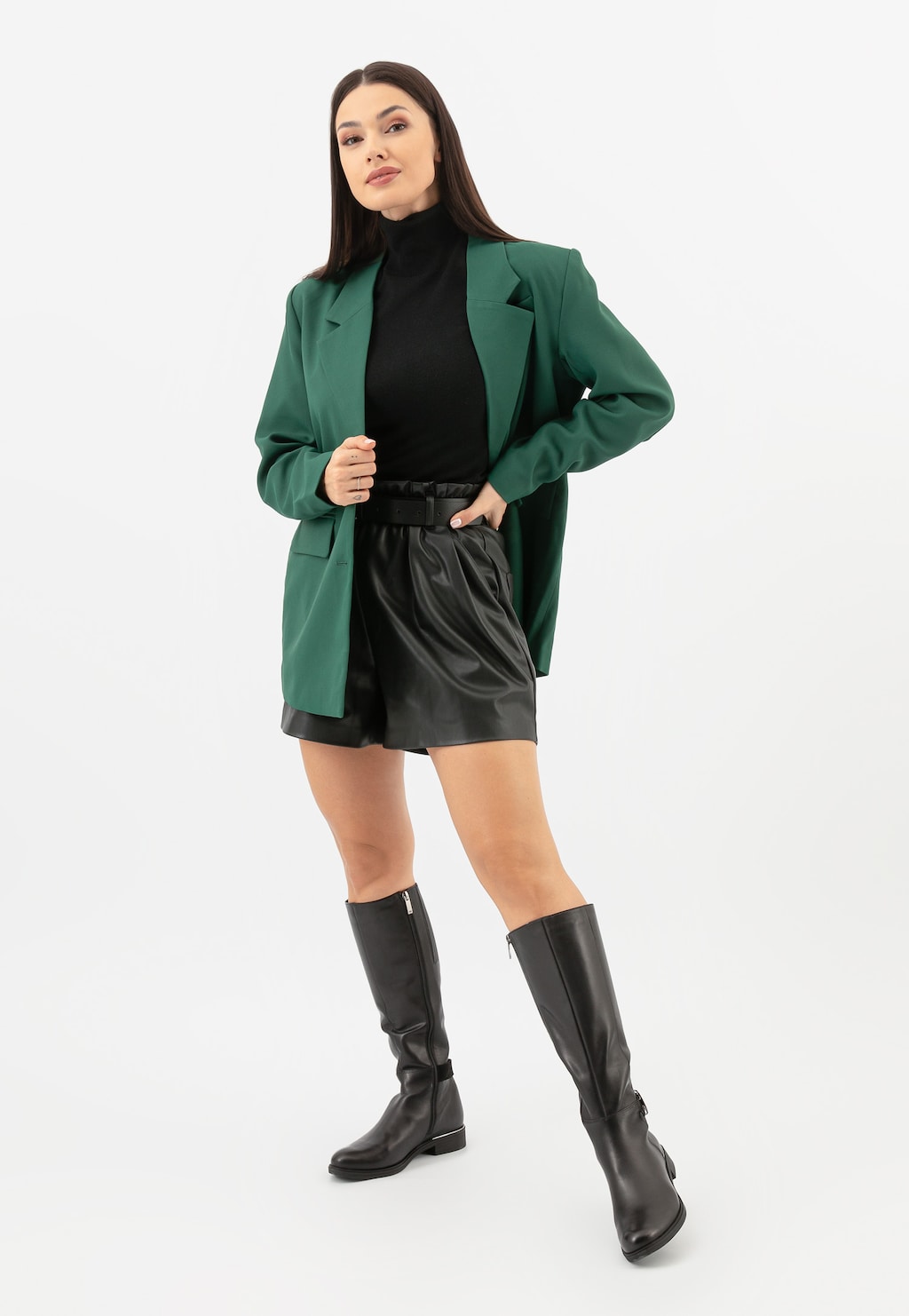 Modelka w zielonej marynarce i czarnych szortach prezentuje eleganckie czarne kozaki damskie typu oficerki Wojas model 71011-71, idealne do stylizacji biznesowych i casualowych.