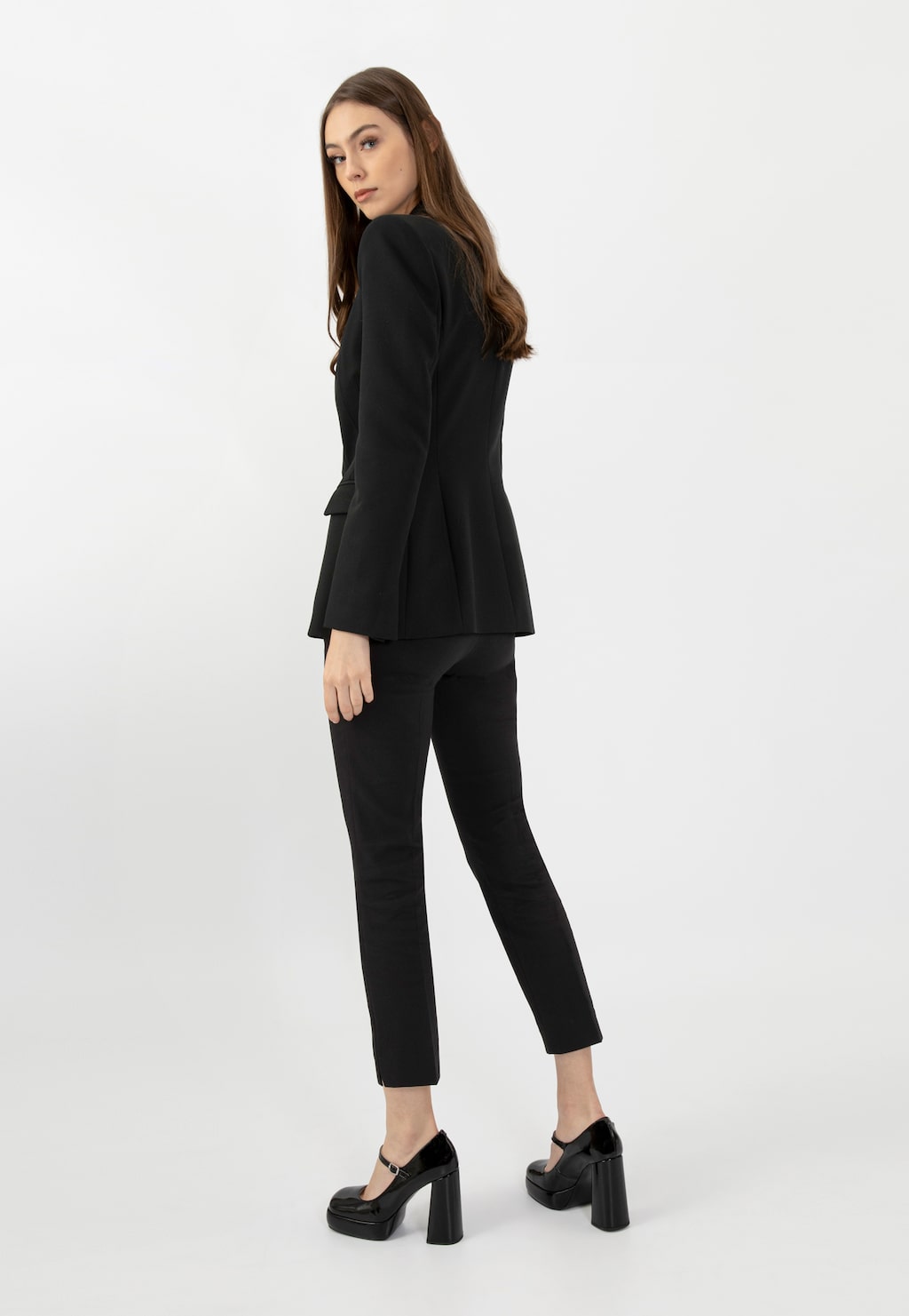 Model w eleganckim czarnym garniturze prezentuje czarne lakierowane czółenka Mary Jane Wojas 35117-31 na wysokim obcasie, ukazując stylowe połączenie klasycznej odzieży z efektownymi butami.