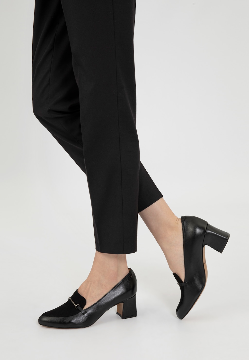 Eleganckie czarne półbuty damskie Wojas model 46014-71 na stabilnym obcasie, ze stylową metalową ozdobą, noszone z czarnymi spodniami, idealne do stroju biznesowego.