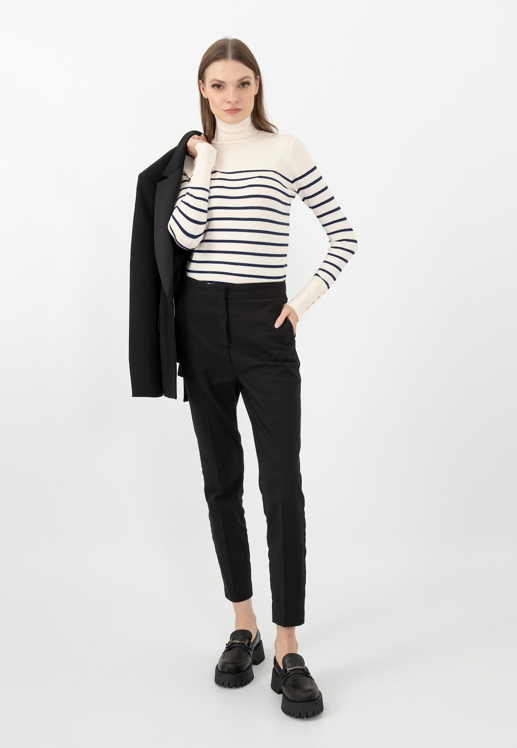 Modelka w eleganckim stroju z czarnymi mokasynami Wojas 46198-51 z metalową ozdobą horsebit. Stylizacja z marynarką, golfem w paski i czarnymi spodniami.