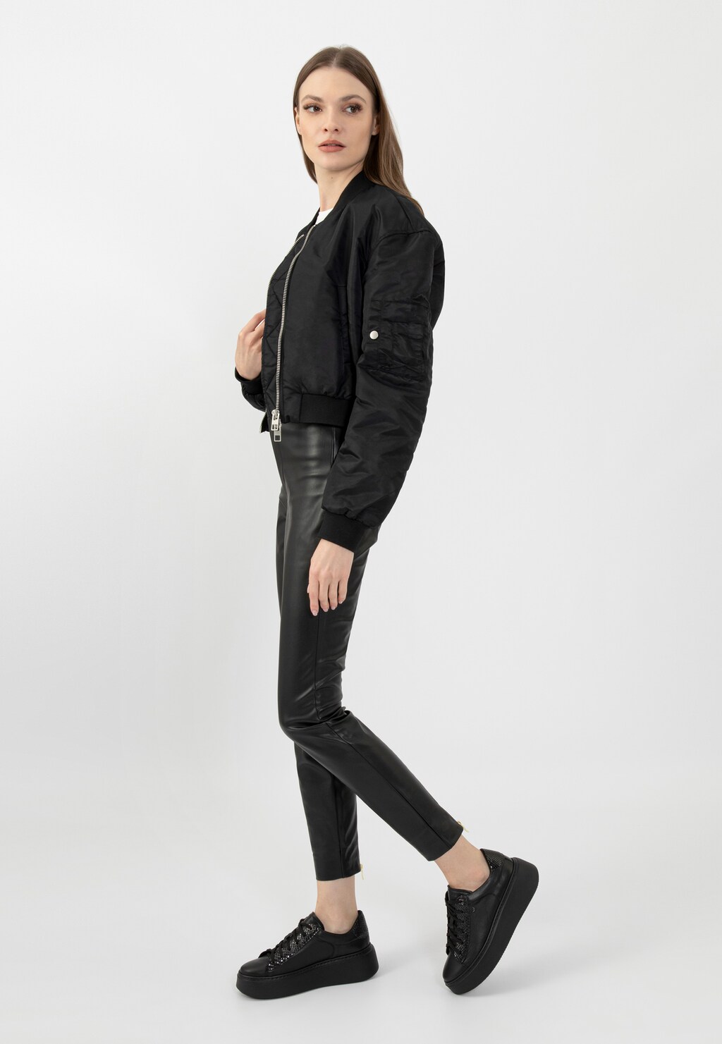 Modelka w czarnej bomberskiej kurtce i skórzanych spodniach prezentuje czarne trampki Wojas na wysokiej platformie model 46246-71, idealne do miejskich stylizacji.