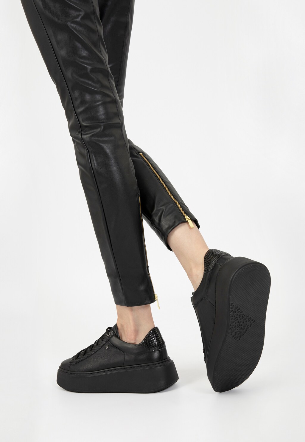 Czarne trampki damskie Wojas 46246-71 na wysokiej platformie widoczne na nodze modelki w czarnych skórzanych spodniach z ozdobnym zamkiem przy kostce.