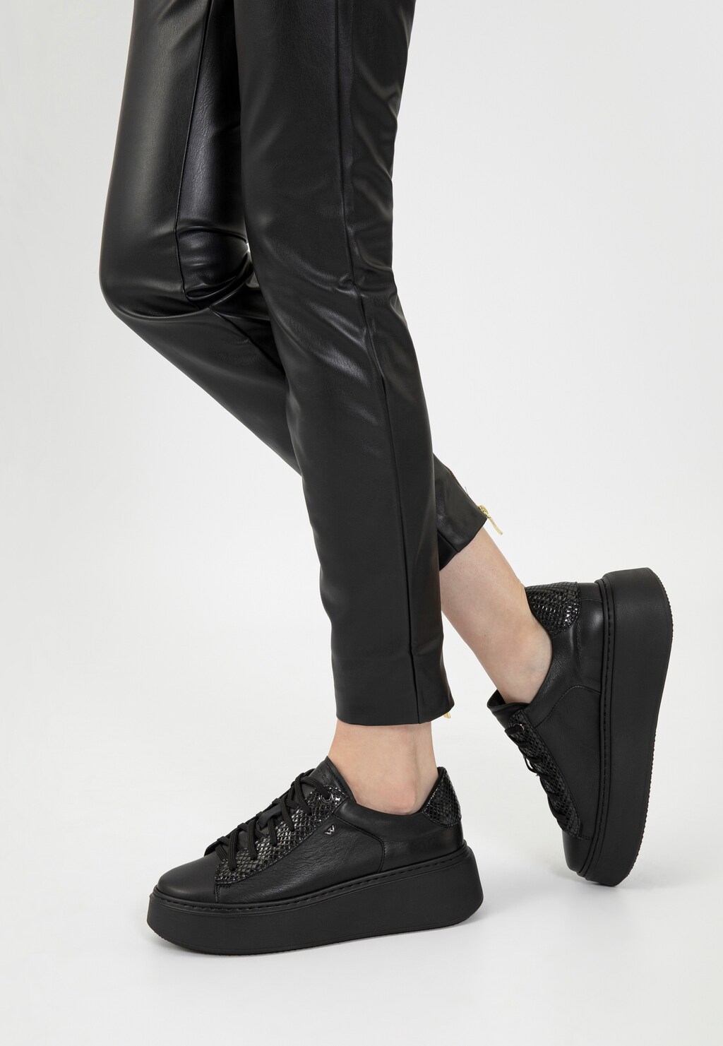 Czarne trampki damskie Wojas 46246-71 na wysokiej platformie zestawione ze skórzanymi spodniami, widok z boku prezentujący modny sportowy design z ozdobnymi elementami.