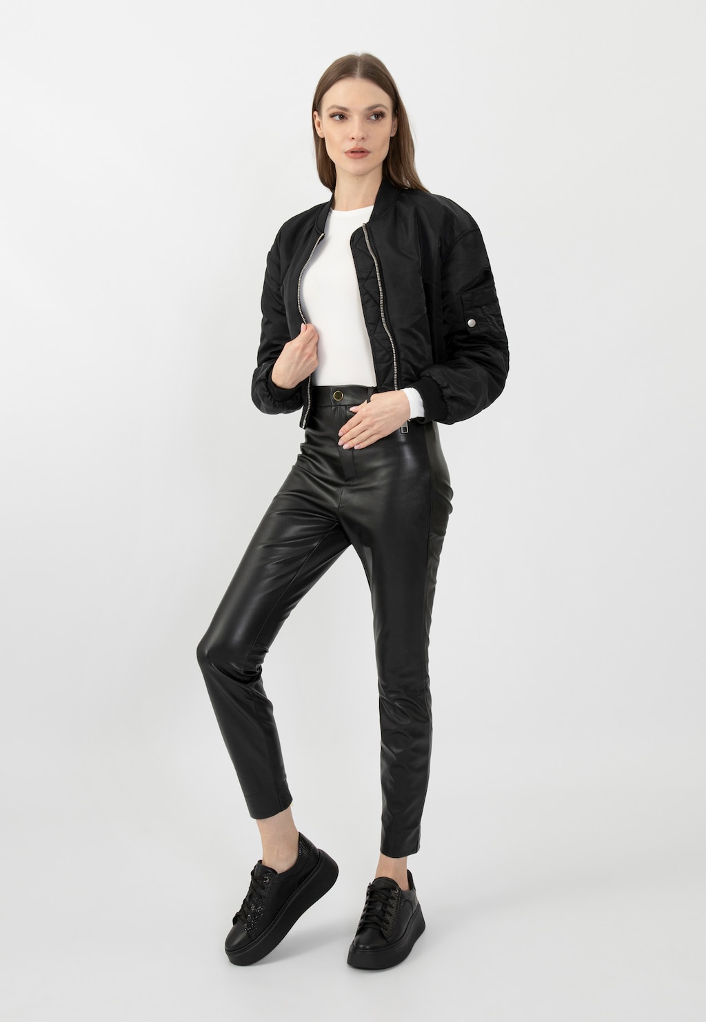 Modelka w czarnej kurtce bomberskiej, białej bluzce i skórzanych spodniach prezentuje czarne trampki Wojas na wysokiej platformie model 46246-71.