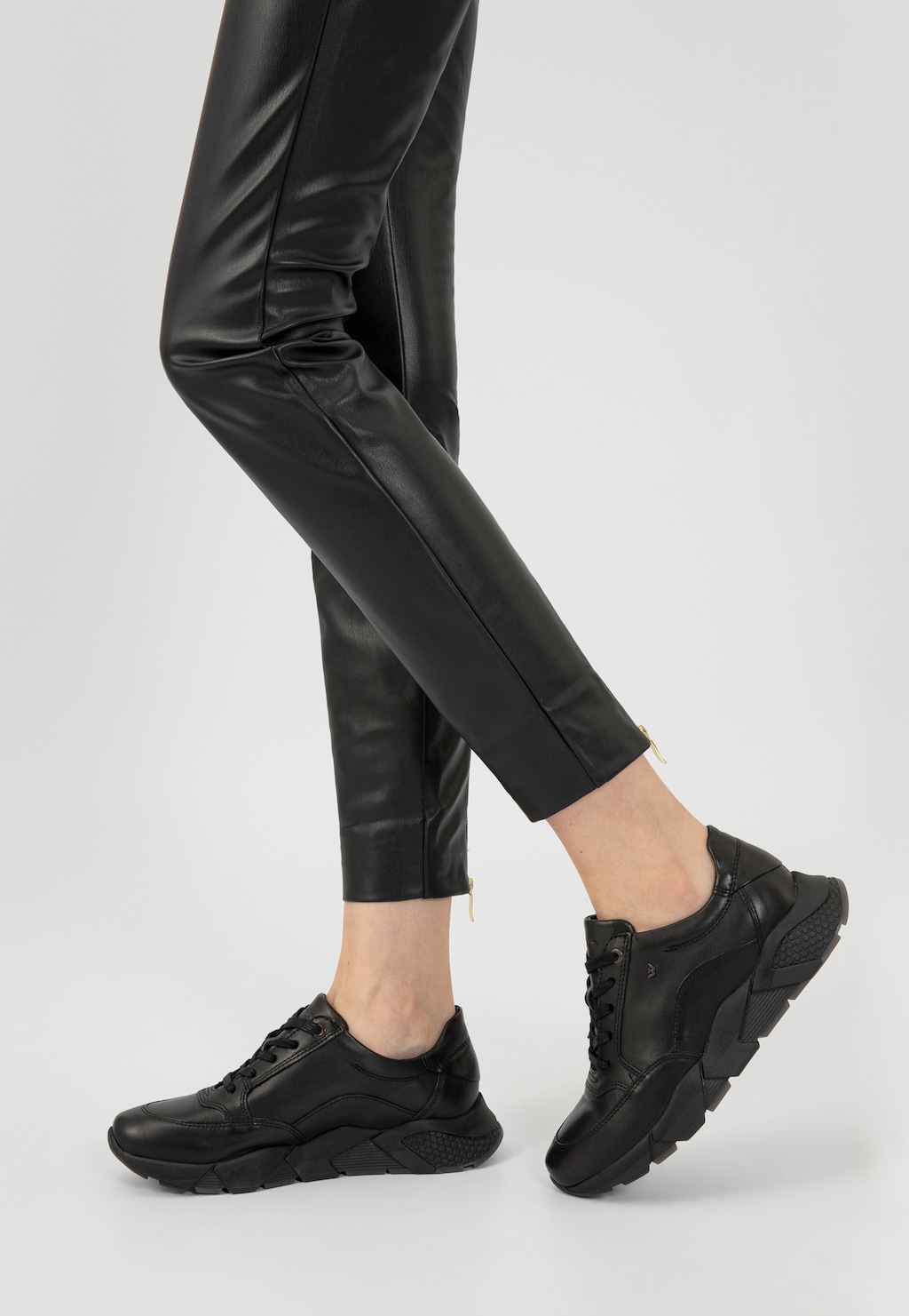 Eleganckie czarne półbuty damskie Wojas model 9406-51 typu sneakers, widoczne na nodze kobiety noszącej skórzane spodnie. Sportowo-elegancki charakter butów z masywną podeszwą.