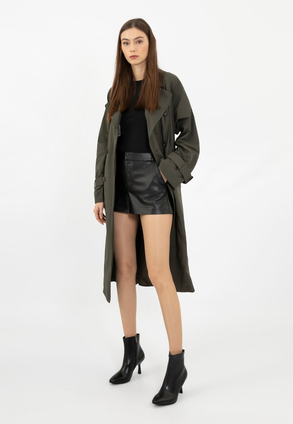 Modelka w stylizacji z czarnymi eleganckimi botkami Wojas 55207-51 na szpilce, czarnej mini spódnicy i oliwkowym płaszczu, prezentująca botki z profilu.