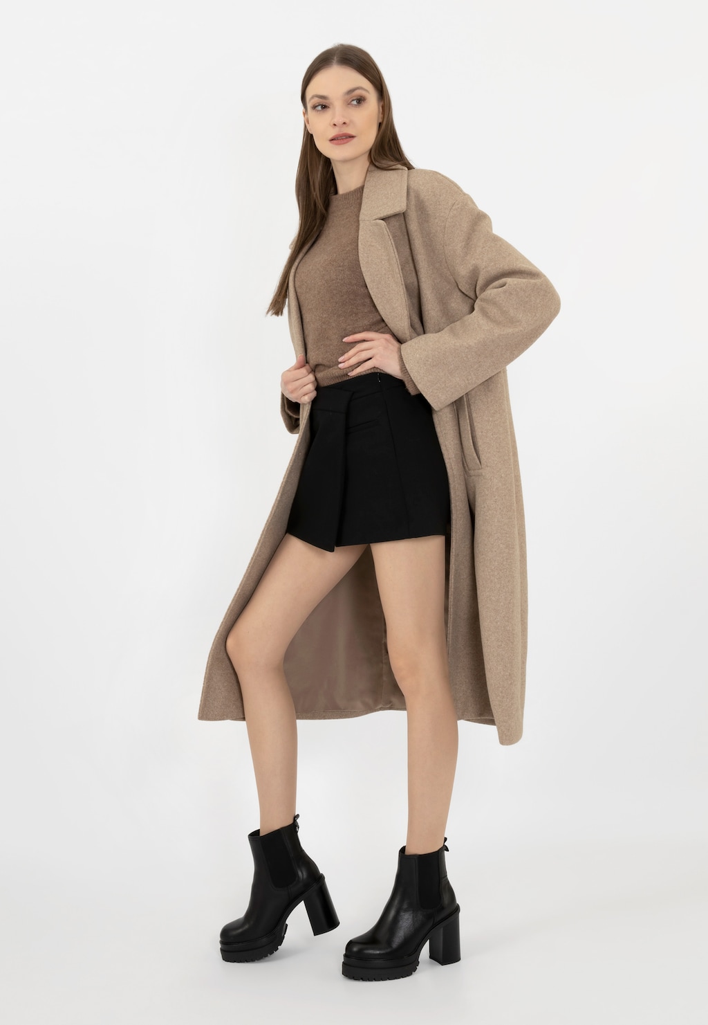 Elegancka stylizacja z czarnymi skórzanymi botkami Wojas model 55223-51 na słupku. Kobieta w beżowym płaszczu, brązowym topie i czarnych szortach prezentuje obuwie na platformie.