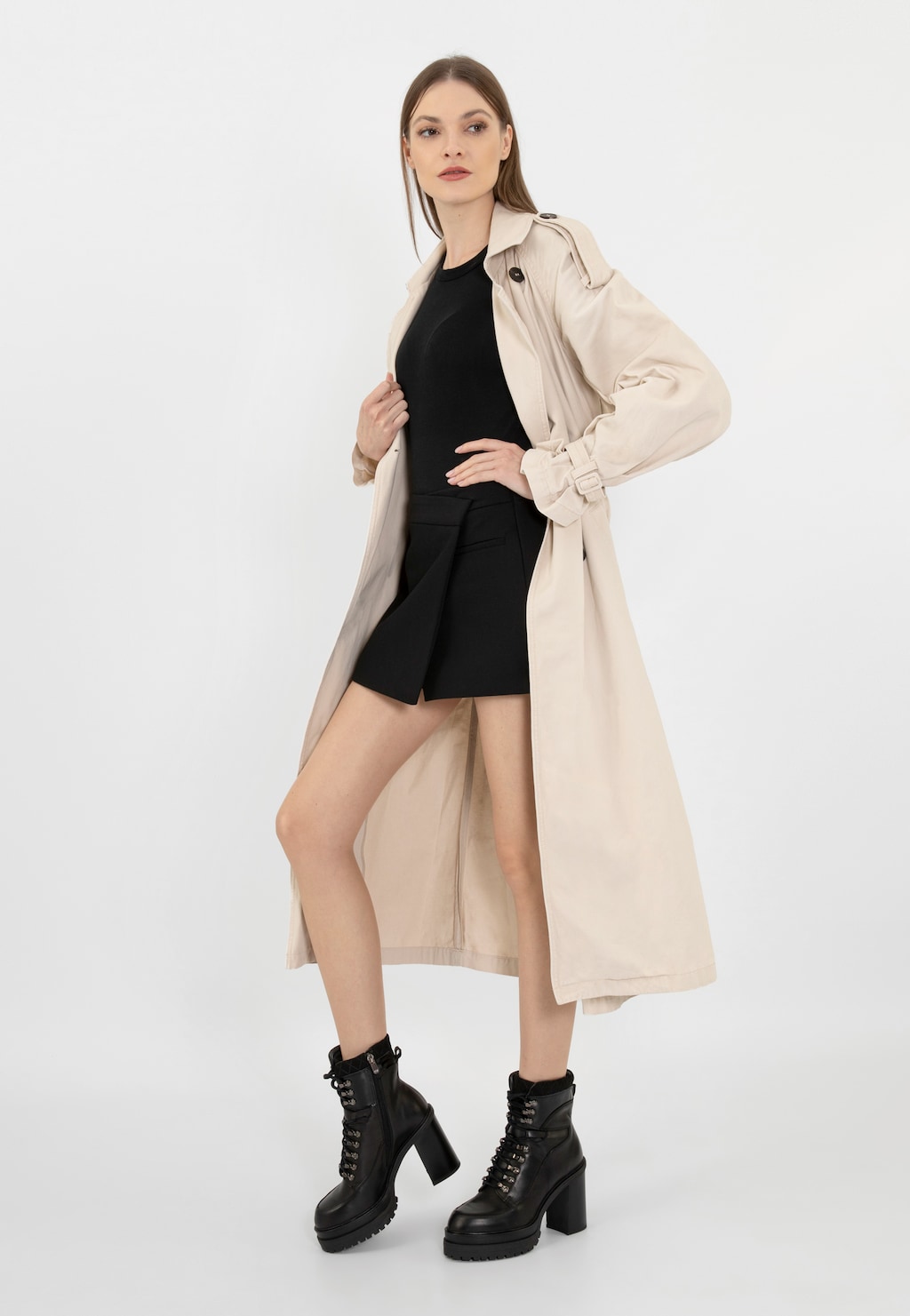 Modelka w beżowym płaszczu i czarnej sukience, prezentująca czarne bikery Wojas model 64104-81 - botki ze skórzanym wykończeniem na masywnym obcasie.