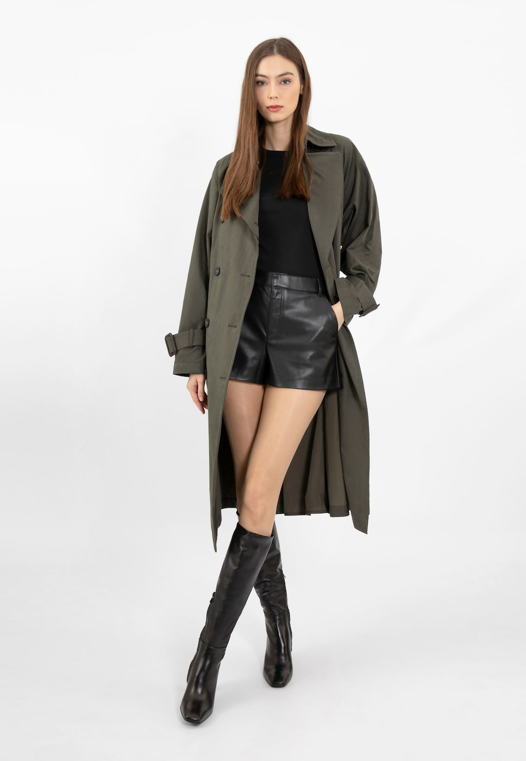 Modelka w stylizacji z czarnymi kozakami Wojas 71044-51 na słupku, w oliwkowym płaszczu i skórzanych szortach. Eleganckie kozaki ze skóry licowej dopełniają jesienną stylizację.