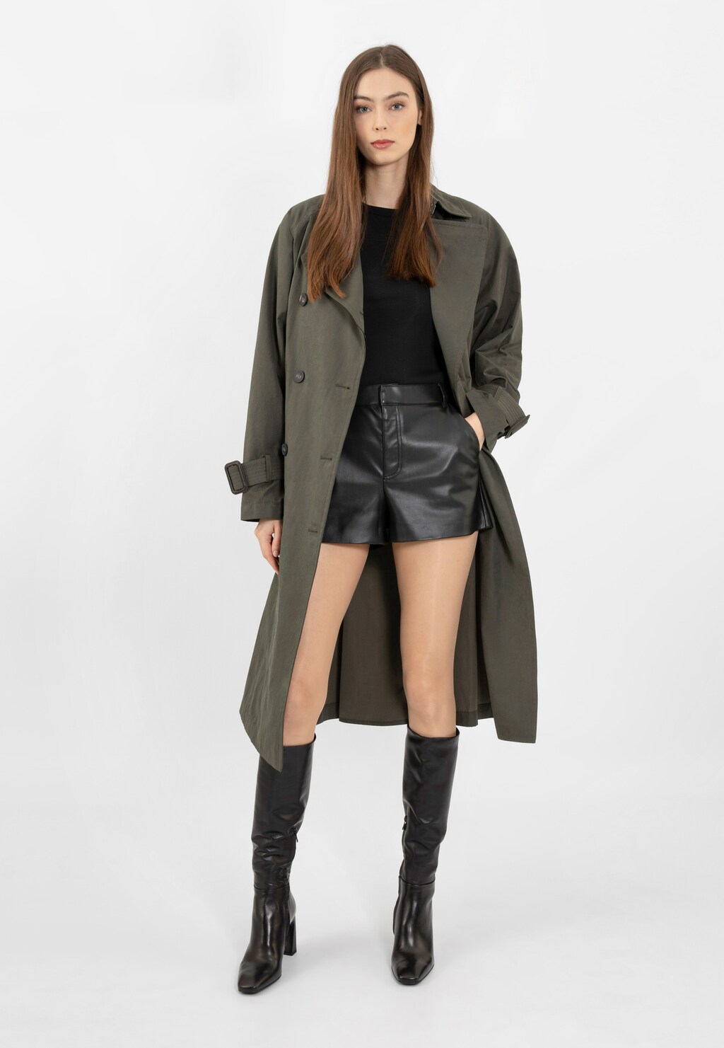 Stylowa modelka w zielonym płaszczu i czarnych szortach, prezentująca eleganckie czarne kozaki damskie Wojas 71044-51 na słupku wykonane ze skóry licowej.