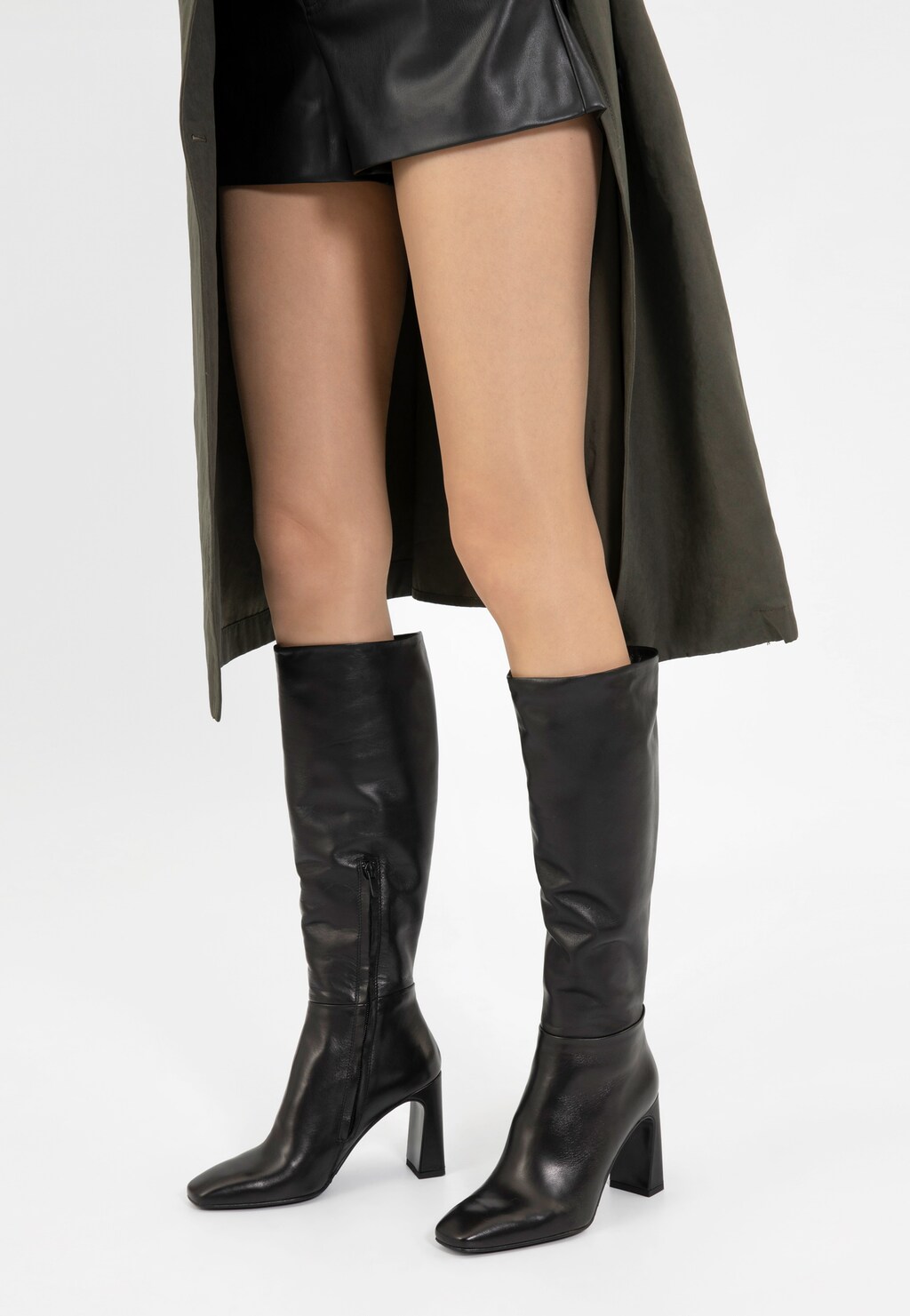 Eleganckie czarne kozaki Wojas 71044-51 ze skóry licowej na modnym słupku. Stylizacja z krótką skórzaną spódnicą i ciemnym płaszczem, pokazująca kozaki do kolana z kwadratowym noskiem.