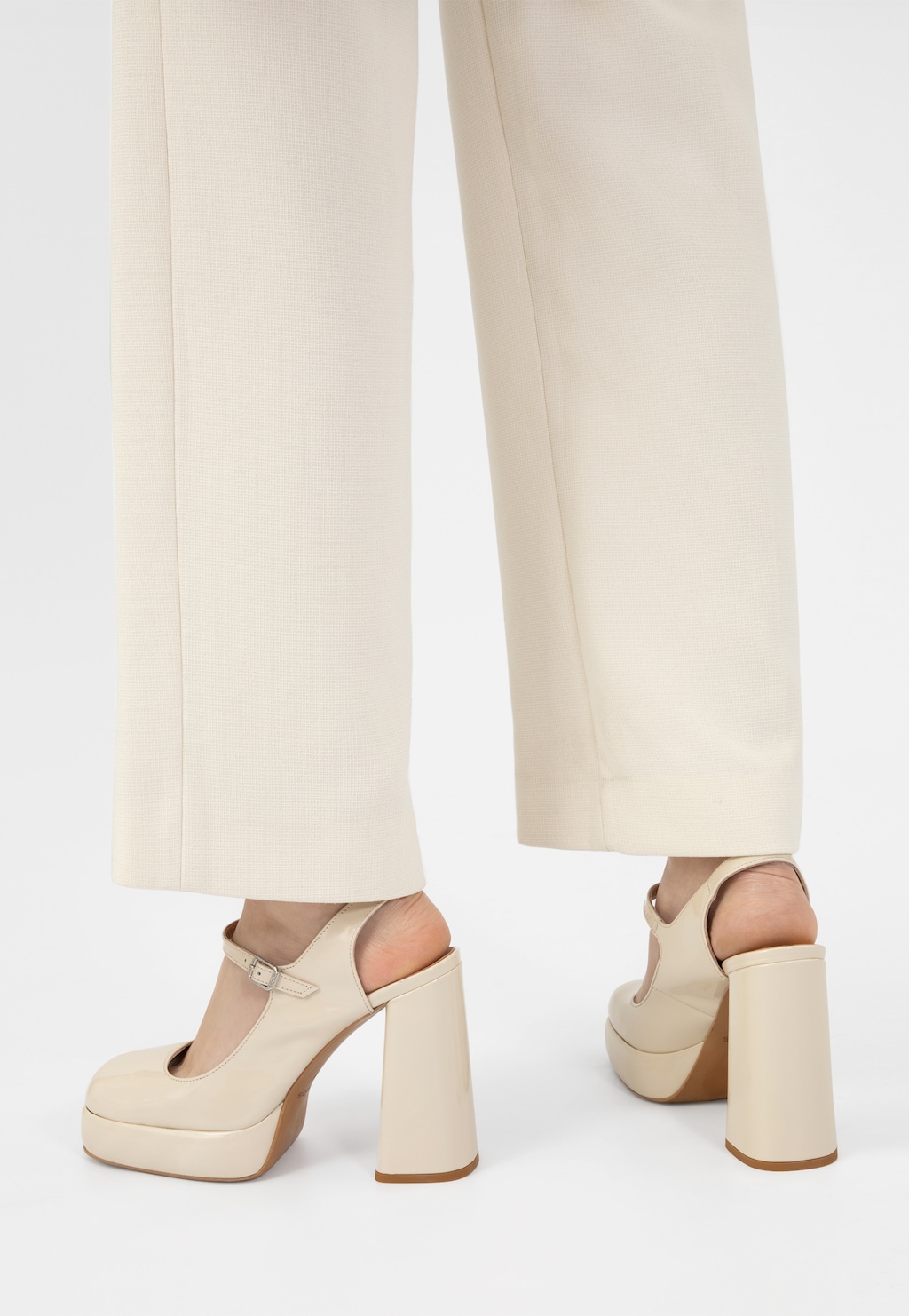 Beżowe czółenka Wojas 35124-34 na masywnym słupku z platformą, widoczne na nogach osoby w jasnych spodniach, prezentujące elegancki profil z charakterystycznym zapięciem na kostce.