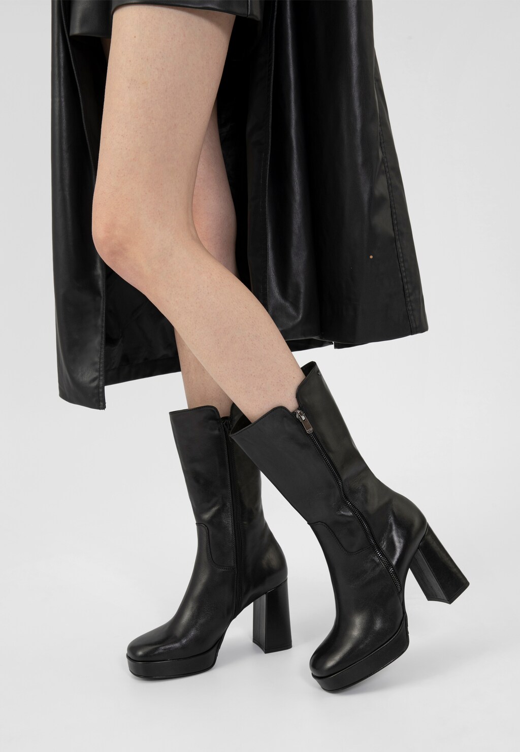 Eleganckie czarne botki damskie Wojas model 55215-51 na wysokim obcasie i platformie, z bocznym zamkiem, noszone do czarnej skórzanej spódnicy.