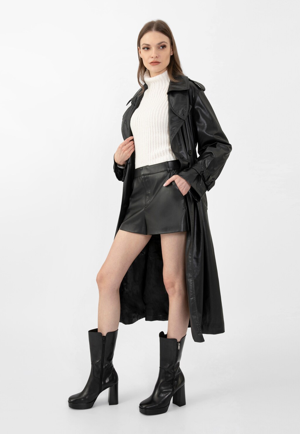 Modelka w stylizacji z czarnymi botkami Wojas model 55215-51 na wysokim obcasie, ubrana w biały golf, czarne szorty i długi skórzany płaszcz.