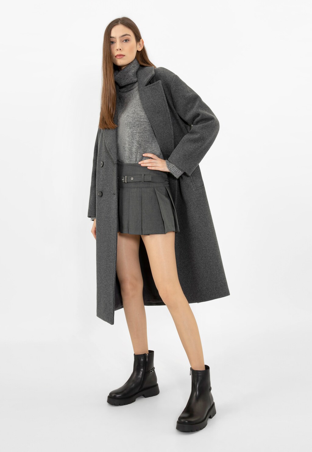 Modelka w szarym płaszczu i spódnicy, prezentująca czarne botki Wojas model 55231-51 ze skóry licowej z metalową ozdobą. Stylizacja uzupełniona golfem i masywną podeszwą butów.