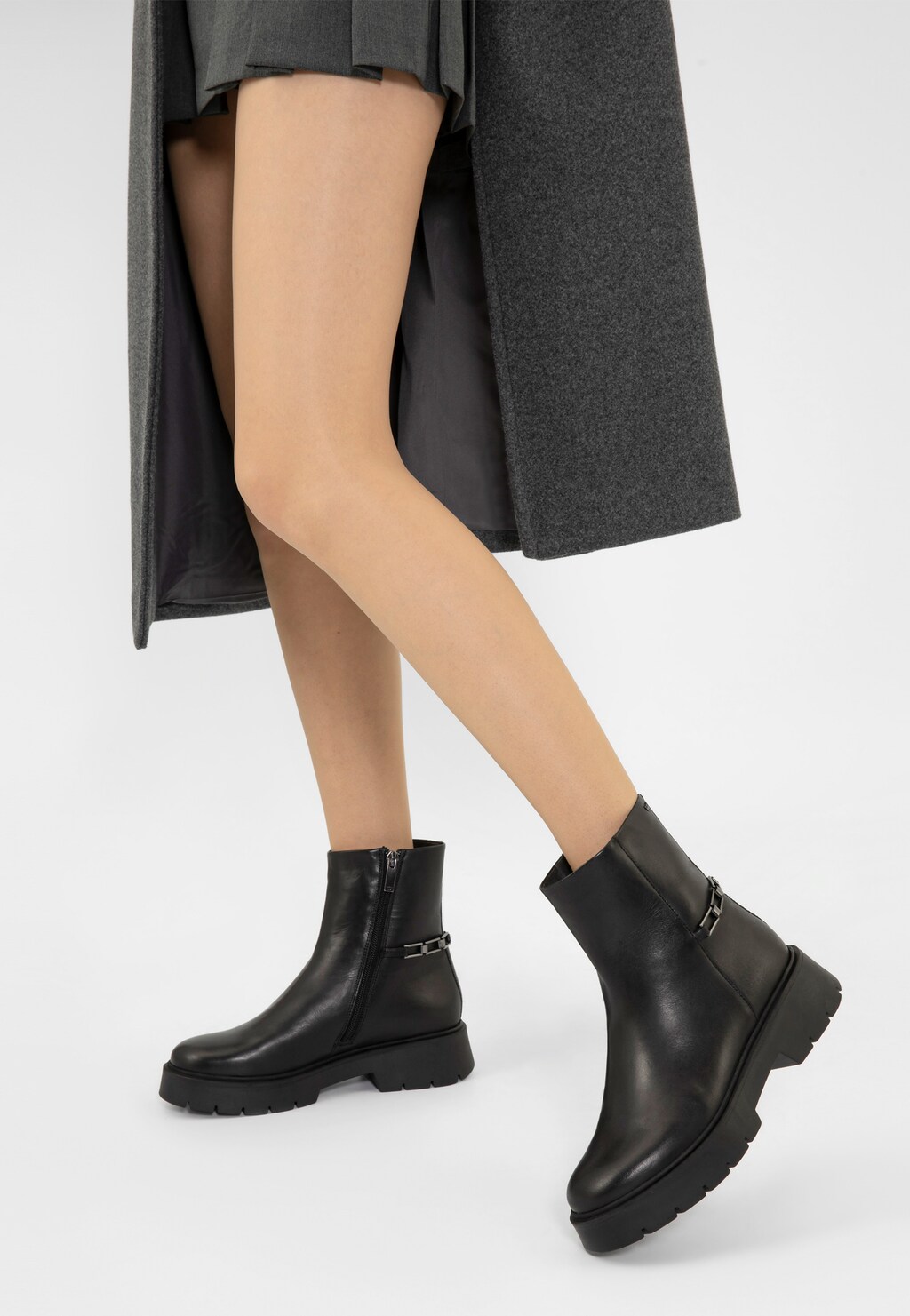 Czarne botki damskie Wojas 55231-51 ze skóry licowej z metalową ozdobą, prezentowane na nodze modelki w szarym płaszczu, z bocznym zamkiem i grubą podeszwą.