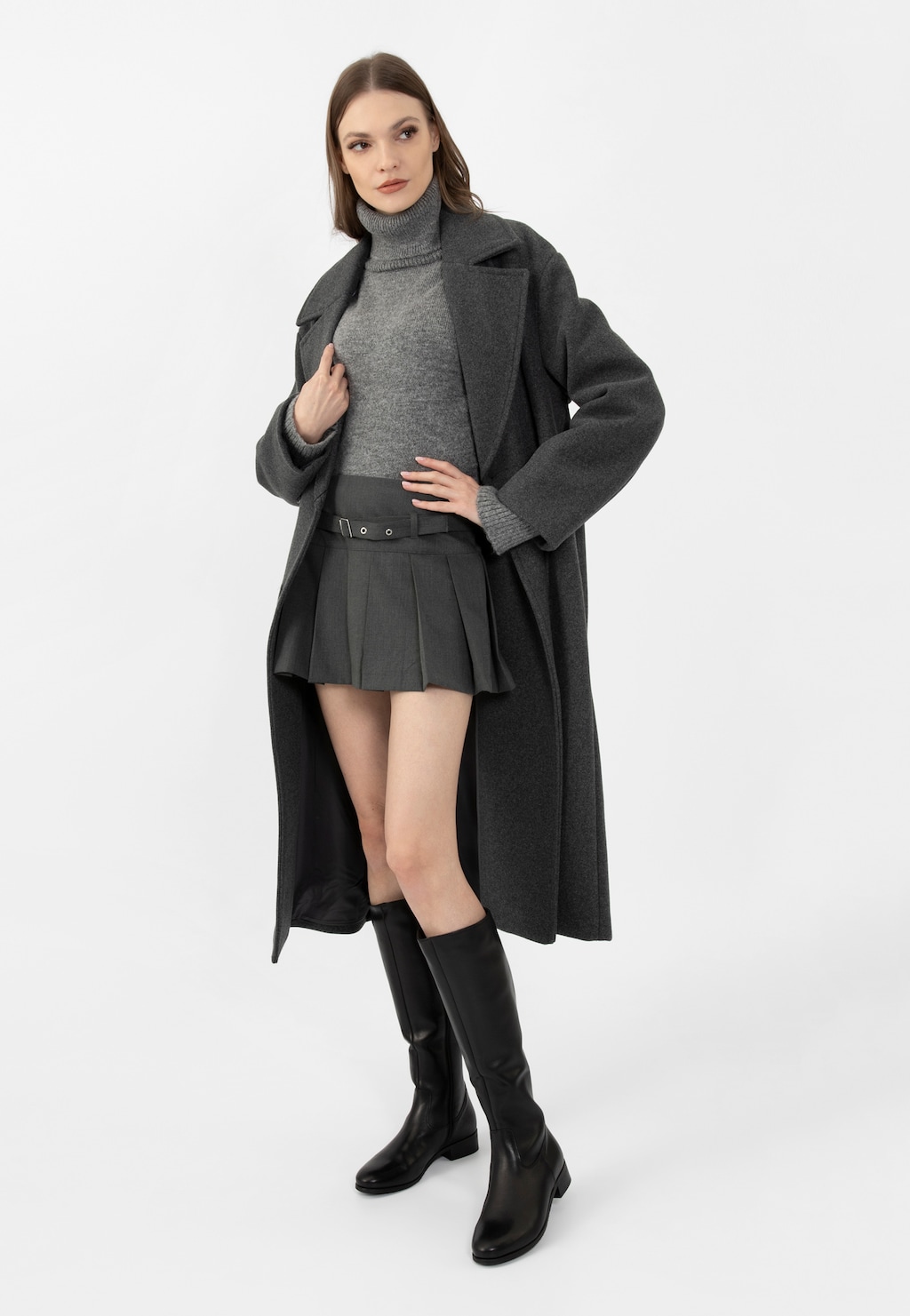 Modelka w szarym płaszczu i golfie prezentuje czarne skórzane kozaki oficerki damskie Wojas model 71015-59, zestawione z krótką plisowaną spódnicą.