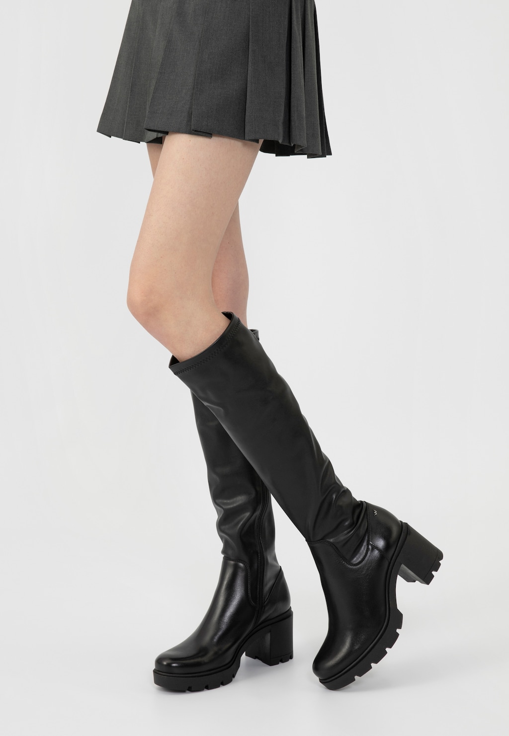 Czarne skórzane kozaki damskie Wojas model 71025-51 na masywnym słupku, prezentowane na nodze modelki w krótkiej plisowanej spódniczce, podkreślające elegancką sylwetkę.