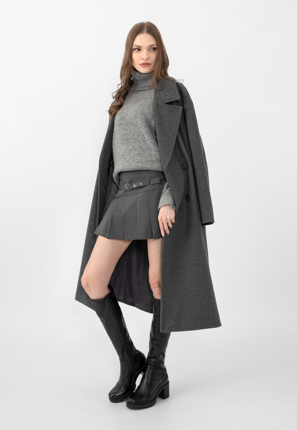 Modelka w szarym płaszczu i golfie, prezentująca czarne skórzane kozaki damskie Wojas 71025-51 na masywnym słupku, zestawione z krótką spódnicą.