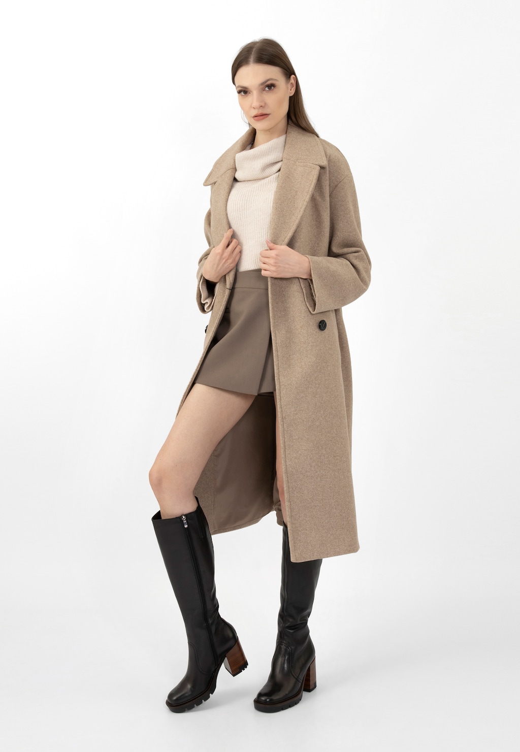 Modelka w eleganckim beżowym płaszczu i jasnym golfie prezentuje czarne kozaki damskie Wojas na słupku model 71050-51, zestawione ze stylową szarą spódniczką.
