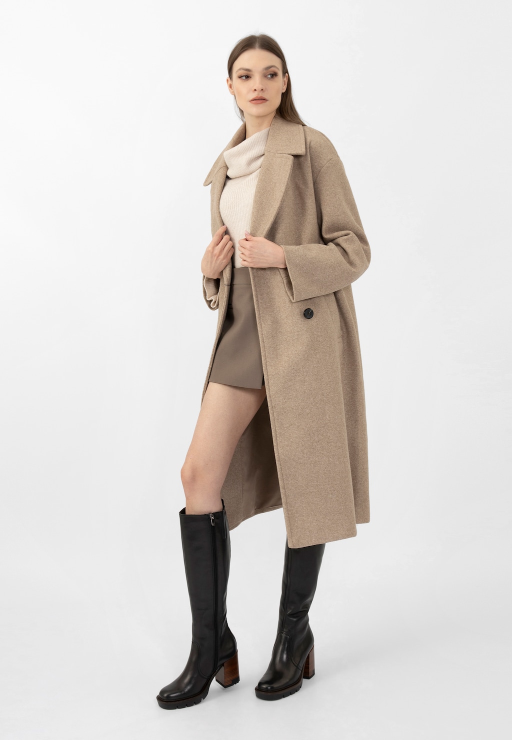 Modelka w beżowym płaszczu i swetrze prezentuje czarne kozaki damskie Wojas model 71050-51 na słupku. Eleganckie obuwie z stabilnym obcasem i grubą podeszwą idealnie uzupełnia jesienną stylizację.