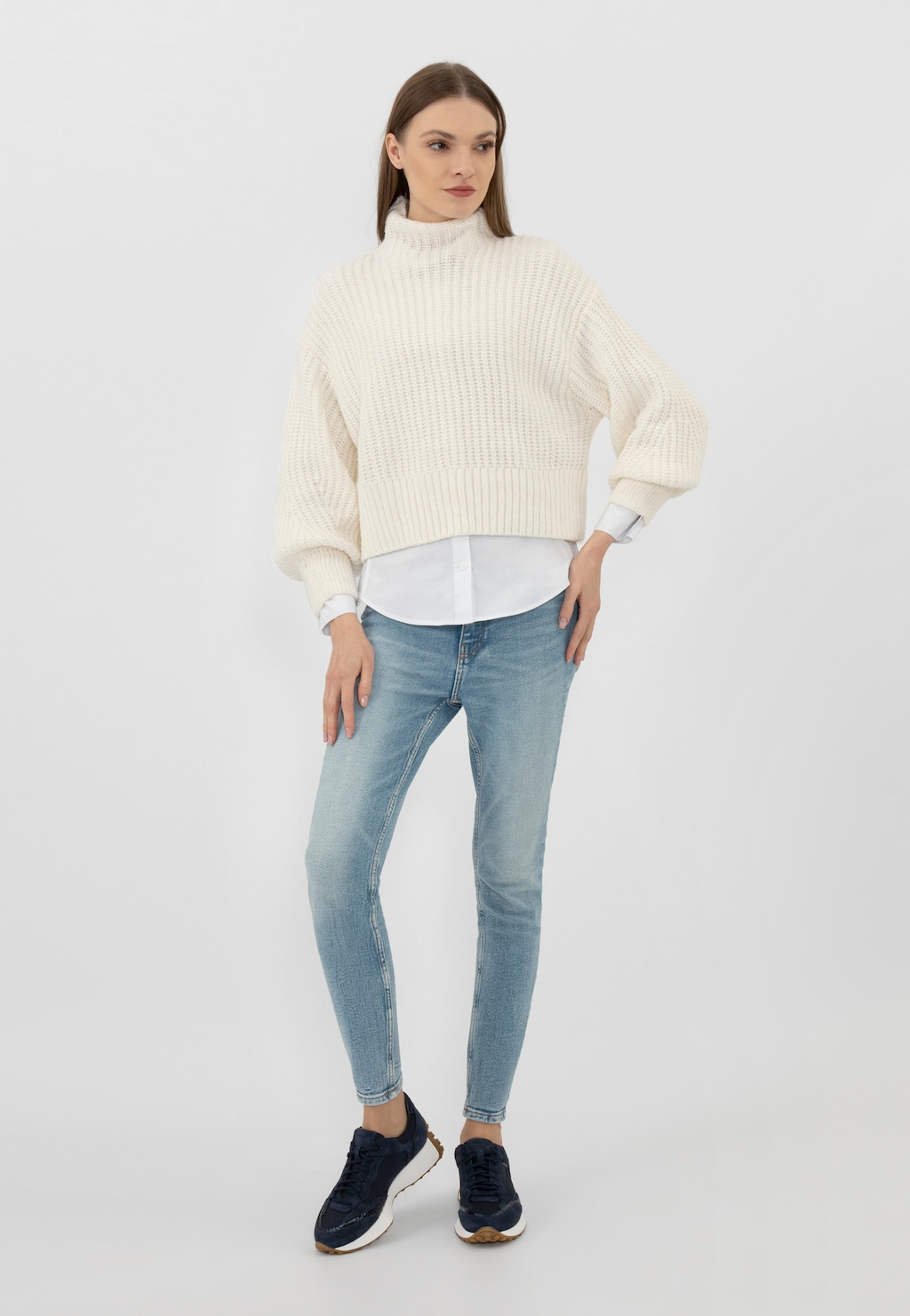 Modelka w stylizacji z kremowym swetrem, białą koszulą i jasnymi jeansami prezentuje granatowe sneakersy damskie Wojas 46245-86 z łączonych materiałów, na jasnej podeszwie.