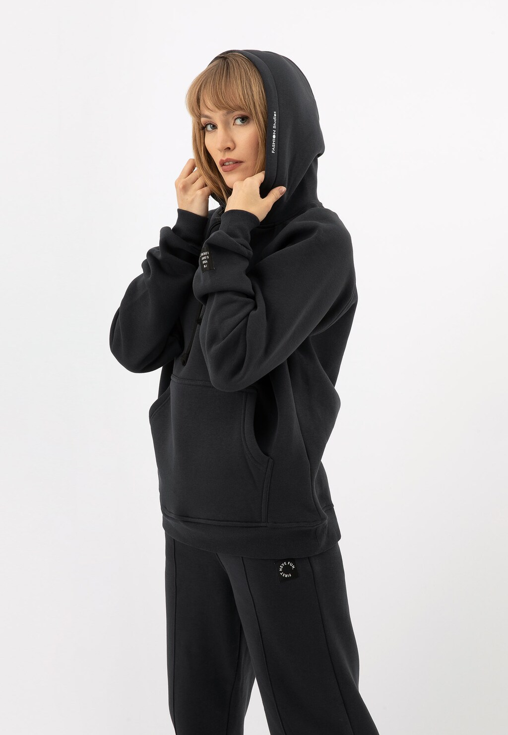 Bluza damska RELAKS w kolorze ciemnego popielu z kapturem, model R98012-11. Przedstawiona na modelce z założonym kapturem, z kieszenią kangurkową z przodu.