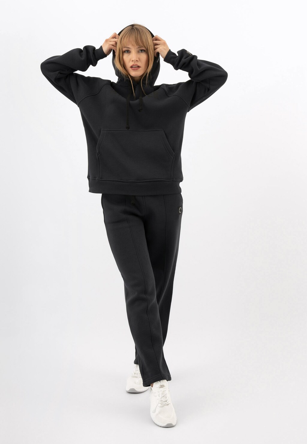 Bluza damska RELAKS model R98012-11 w kolorze ciemnego popielu z czarnym napisem, prezentowana z dopasowanymi spodniami i białymi butami sportowymi, kaptur założony.