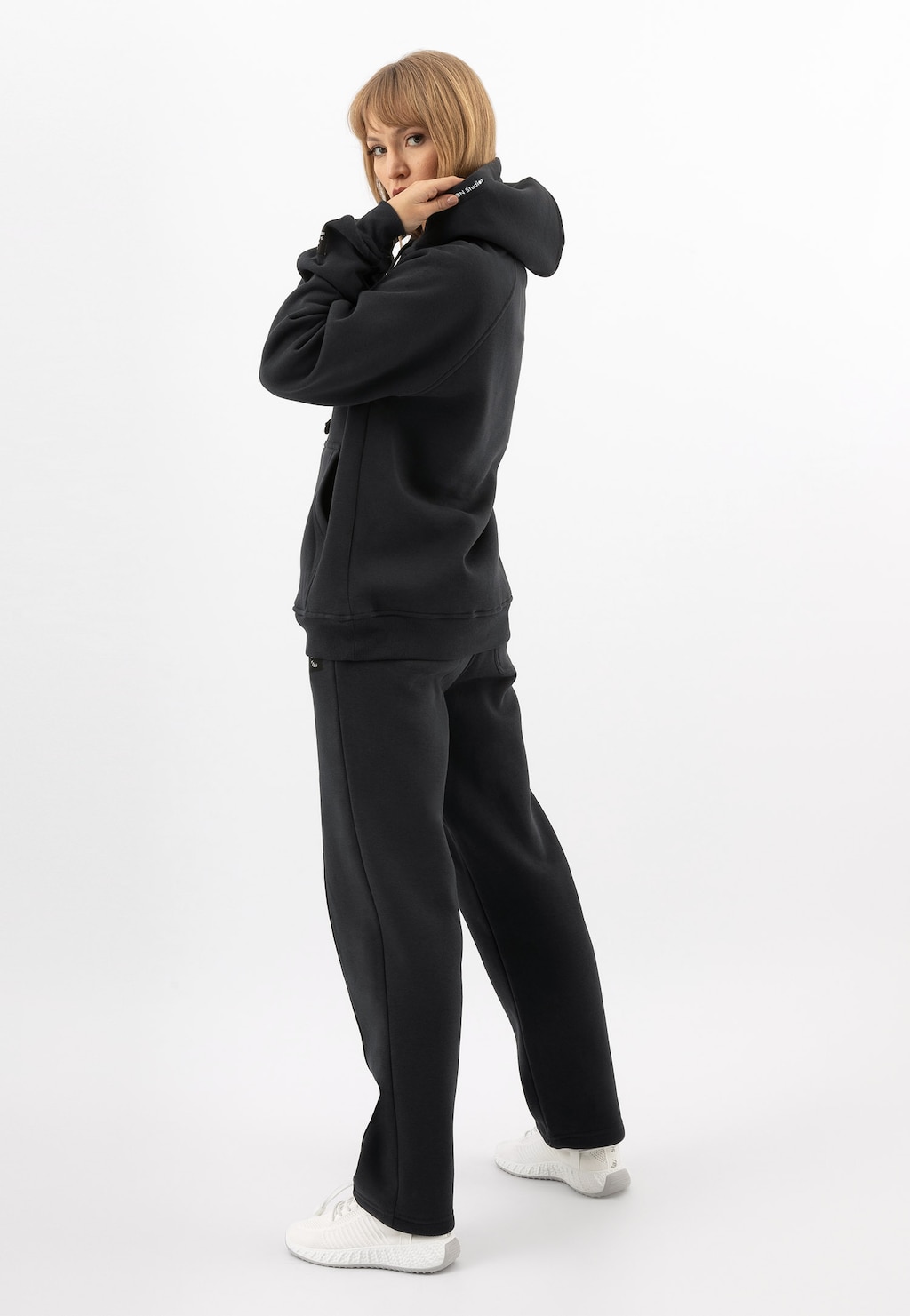 Bluza damska RELAKS model R98012-11 w kolorze ciemnego popielu z kapturem, prezentowana w komplecie z dopasowanymi spodniami i białymi butami, widok z profilu.