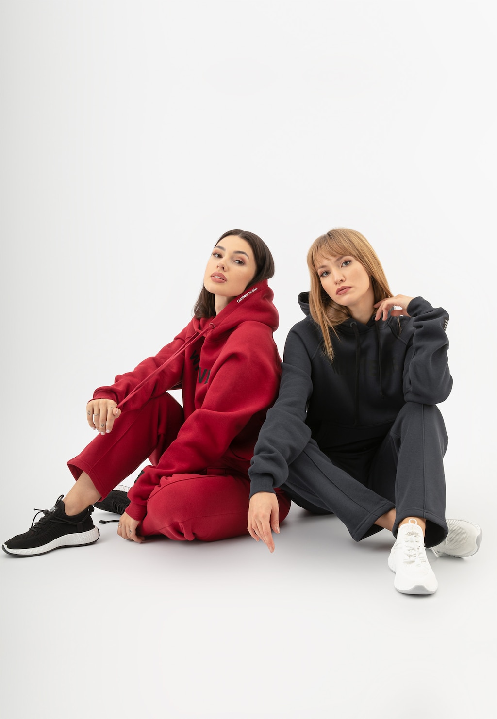Czerwone spodnie dresowe marki Relaks model R98013-15 o prostym kroju prezentowane przez dwie modelki w zestawie z bluzami z kapturem w kolorach czerwonym i czarnym.