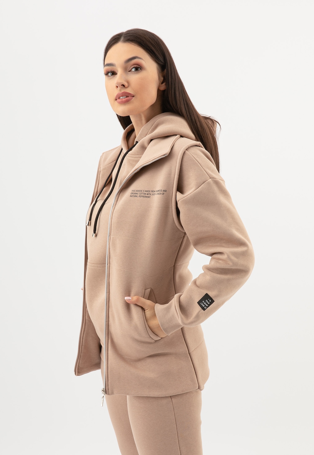 Beżowa kamizelka dresowa RELAKS model R98020-14, z kapturem i kieszeniami, prezentowana w ujęciu bocznym. Widoczne zapięcie na zamek i małe logo na rękawie.