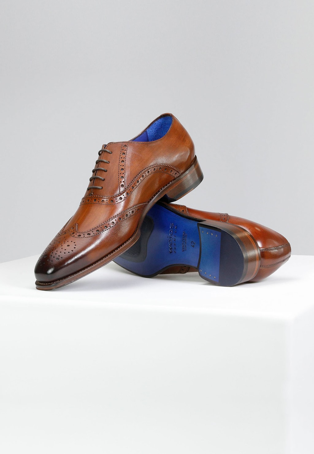 Eleganckie oxfordy męskie Wojas PREMIUM 10061-52 w jasnobrązowym kolorze z niebieską podeszwą, zdobione ażurowymi wzorami brogues, ukazane z boku i od spodu.